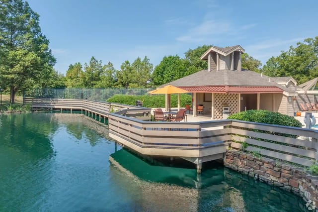 Lakeside outdoor pavilion with a wooden deck, orange umbrella, and seating by the water.