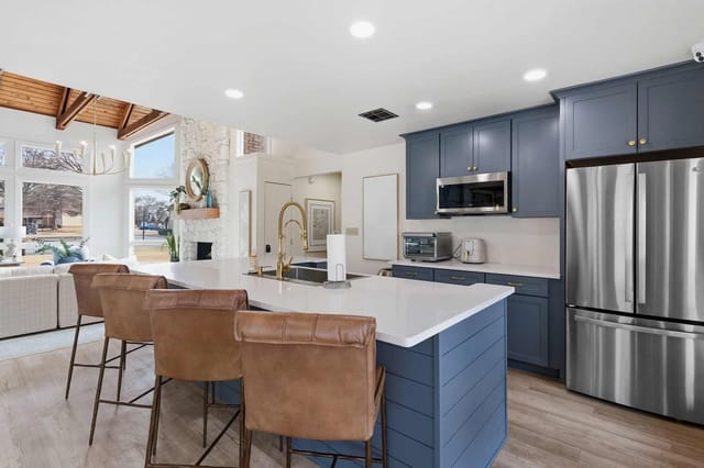 Modern blue kitchen with island, stainless appliances, and bright open living area.