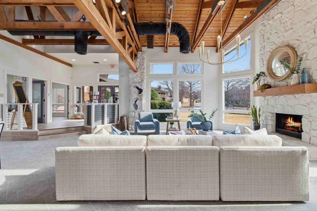 Spacious resident lounge with a stone fireplace, vaulted wooden beams, and large windows.