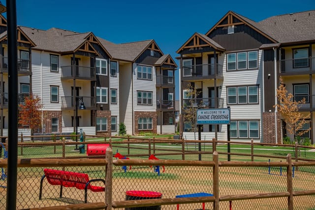 Exterior of a multi-building apartment community with a fenced dog park and playground.