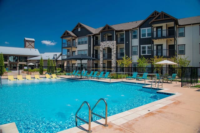 Outdoor community pool with blue water, lounge chairs, and an apartment building in the background.