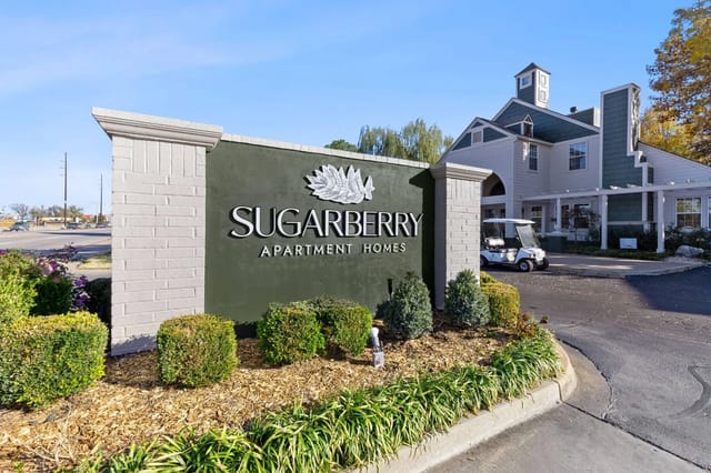 Exterior Sugarberry Apartment Homes sign with landscaping and building in background.