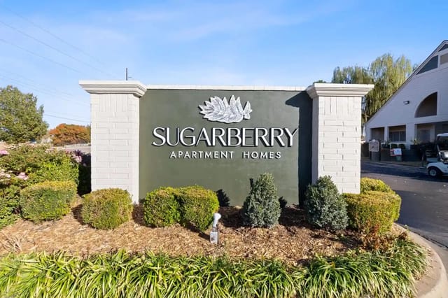 Entrance sign for Sugarberry Apartment Homes with landscaped shrubs.
