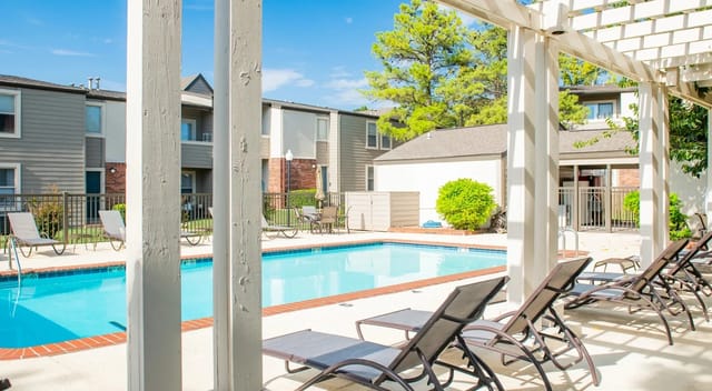 Outdoor apartment community pool with lounge chairs under a white pergola.