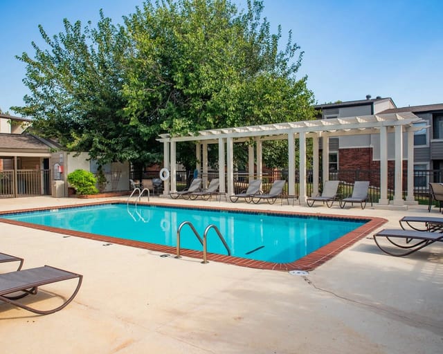 Outdoor apartment community pool with lounge chairs under a pergola.