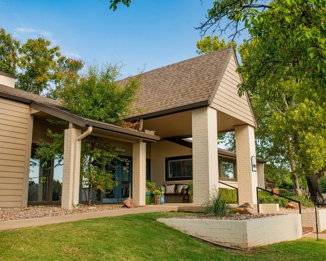 Exterior entrance to apartment community with a covered porch and landscaped surroundings.
