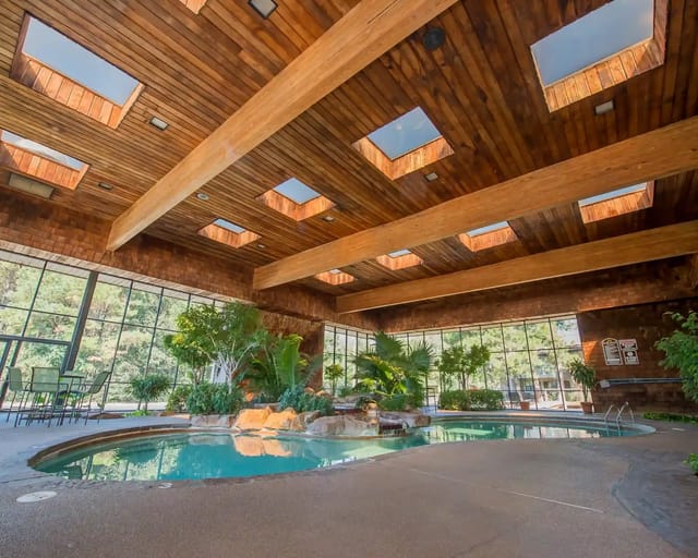 Indoor community pool area with glass walls, skylights, and wooden beams.