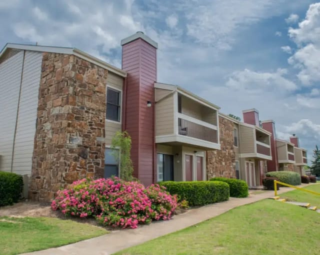 Exterior view of apartment buildings with stone accents, balconies, and landscaped grounds.