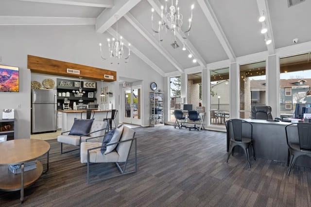 Bright community lounge with high ceilings, chandeliers, large windows, seating and a kitchenette.