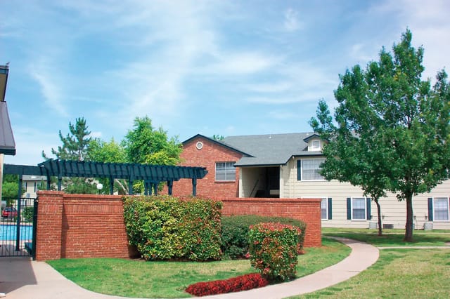 Exterior view of a brick apartment building with landscaping and a curved walkway.