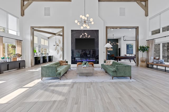 Spacious lounge area with a modern fireplace, two green sofas, and a billiards table visible in the background.