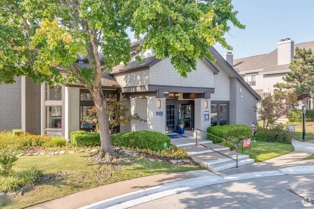Exterior view of a modern apartment community building with entrance, steps, and landscaped grounds.