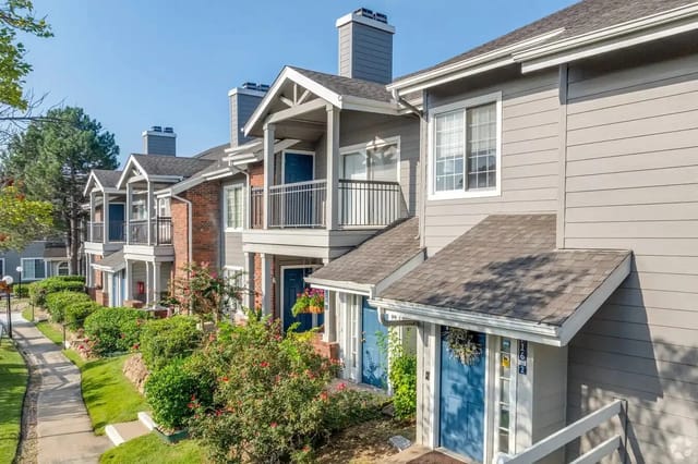 Row of townhouse-style apartment buildings with blue doors, balconies, and landscaped path.
