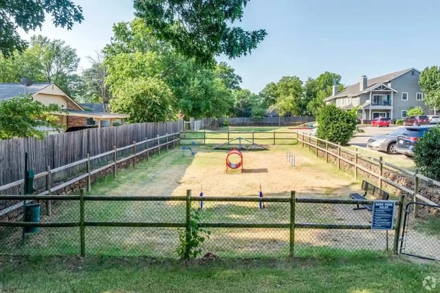 Fenced playground with sand and play structures in a residential community.