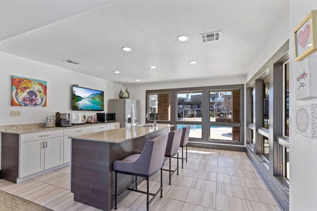 Modern communal kitchen with island, granite counters, bar seating, and pool-view windows.