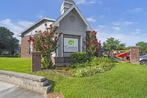 Exterior entrance sign for a multifamily community with landscaped shrubs and brick pillars.