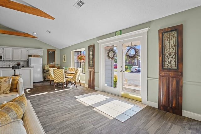 Bright communal living area with a kitchen, dining table, and glass doors.