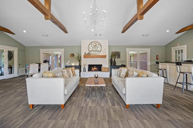 Spacious communal lounge with two gray sofas around a coffee table, a fireplace, chandelier, and bar seating.