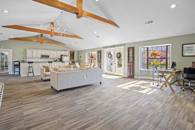 Bright communal lounge with sofas, a kitchen bar, and a work desk in a clubhouse.