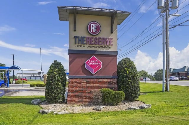 Exterior monument sign for The Reserve at Elm Urban Apartments with surrounding landscaping.