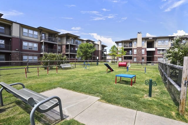 Shared courtyard with playground equipment and benches among mid-rise apartment buildings.
