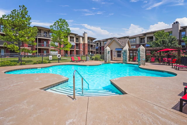 Resort-style swimming pool with lounge chairs and apartment buildings in the background.