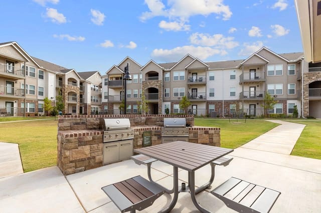 Outdoor grilling station with picnic table in front of apartment buildings.