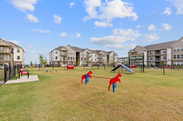 Dog park with agility equipment and apartment buildings in the background.