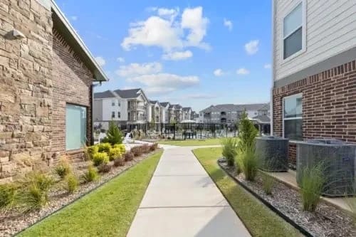 Sidewalk leading to apartment buildings with a pool and courtyard in the background.