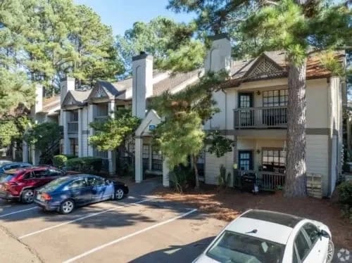 Exterior view of a multifamily apartment building with a parking lot and trees.