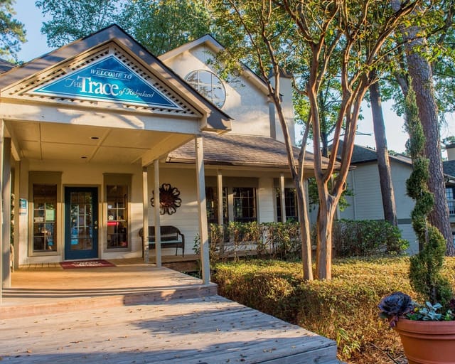 Exterior entrance to The Trace of Ridgeland apartment community with sign, porch, and trees.