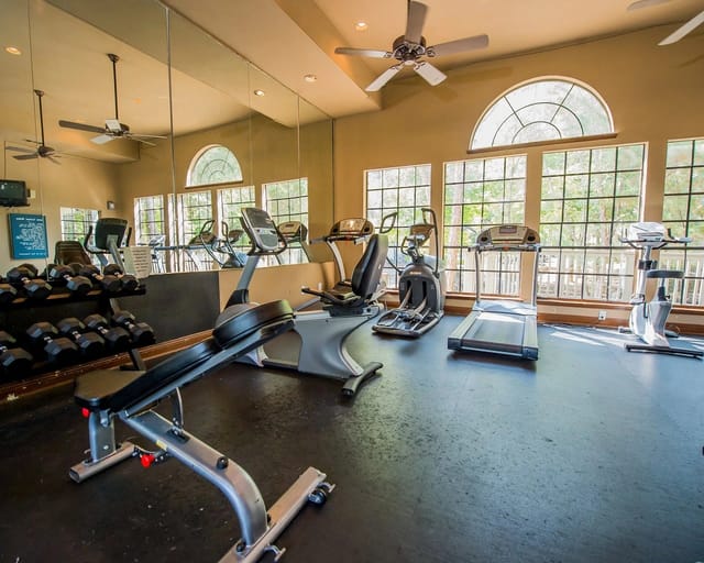 Fitness center with treadmills, ellipticals, weights, and mirrors.