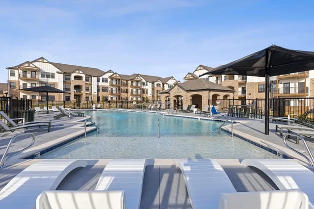 Outdoor pool at a multi-family apartment community with lounge chairs and umbrellas.