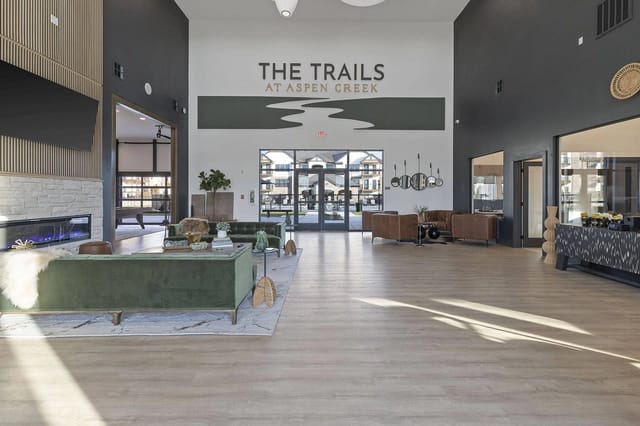Modern apartment lobby with green sofas and a sign reading 'The Trails at Aspen Creek'.