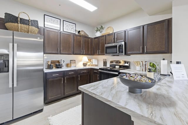 Modern kitchen with dark wood cabinets, stainless steel appliances, and a marble island.