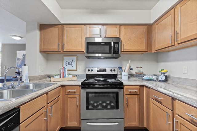 Kitchen with light wood cabinets, stainless steel appliances including a microwave and stove, and a sink.
