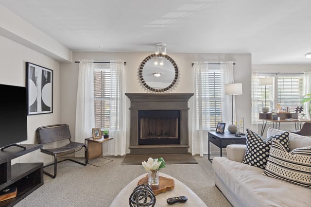 Modern living room with a gray fireplace, a large round mirror above it, and a plush sofa.