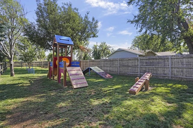 Playground with slide and climbing ramp in a grassy, fenced yard.