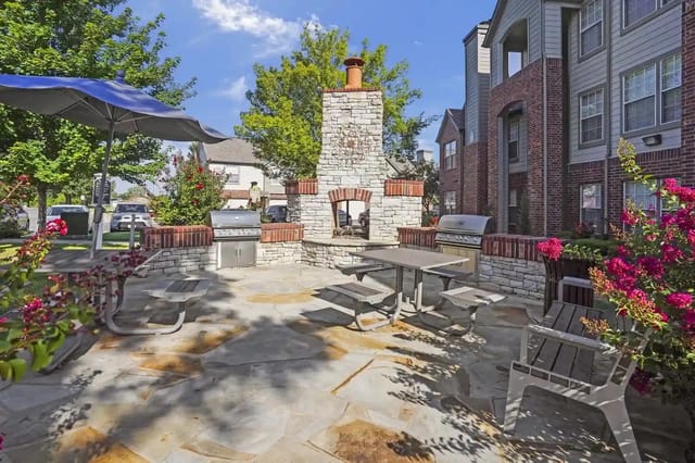 Outdoor community grilling area with a stone chimney, built-in grills, and picnic tables.