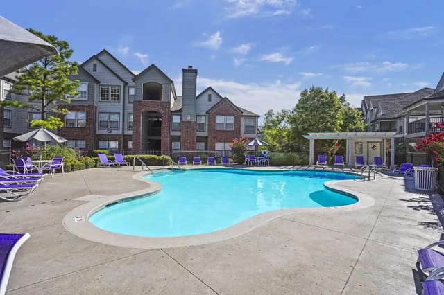 Outdoor apartment pool area with curved pool, purple lounge chairs and umbrellas