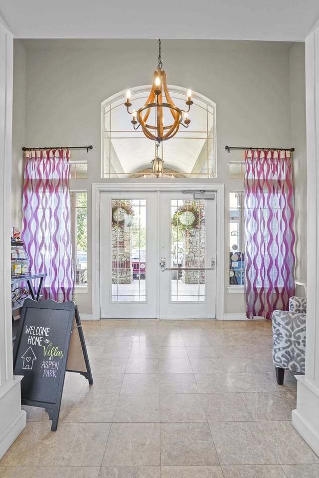 Lobby entry with double glass doors, purple curtains, and a chandelier.