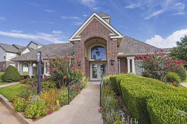 Exterior view of a brick apartment community with a landscaped walkway and colorful flowers.