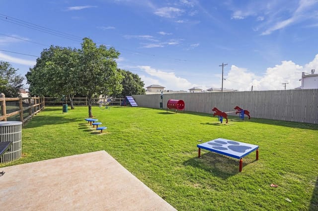 Fenced grassy community playground with a slide, seesaw, and climbing toys.