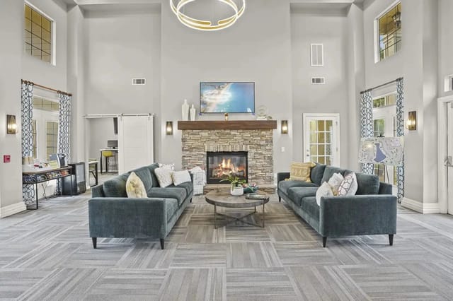 Lobby-style communal lounge with two teal sofas, a stone fireplace, and a mounted TV.