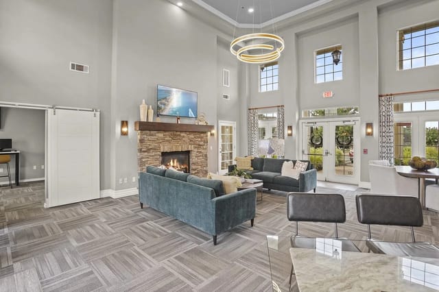 Spacious modern resident lounge with a stone fireplace, teal sofas, and large windows.