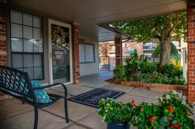 Entrance to an apartment building with a glass door, bench, and landscaped plantings.