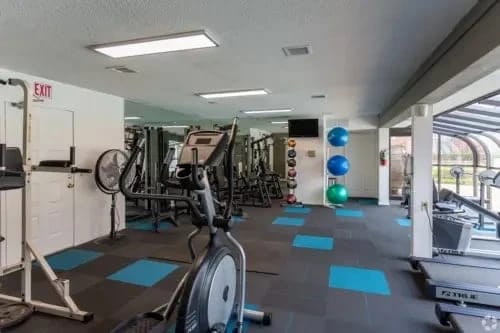 Inside a modern apartment community gym with treadmills, weights, and blue-tiled flooring.