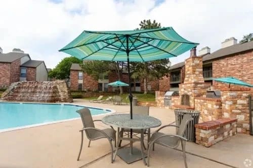 Outdoor community pool area with seating, umbrellas, and brick accents.