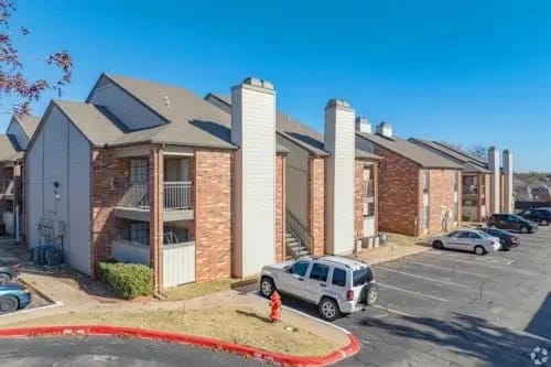 Exterior view of a brick apartment complex with multiple entrances, a parking lot, and clear blue sky.