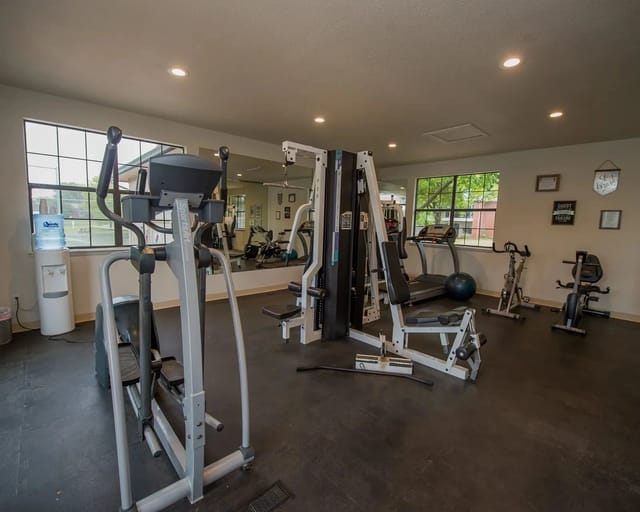 Well-lit gym with cardio and weight machines, mirrors, and a water cooler.